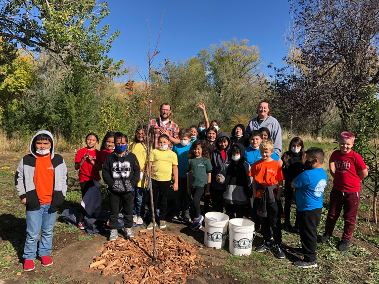 Sam and fourth graders from Pacific Heritage Academy stand together around a tree they planted.