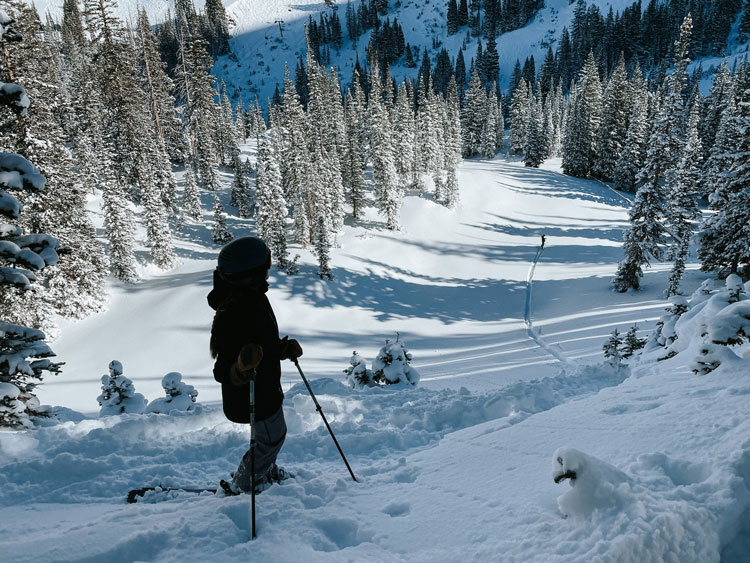 Ayja stands at the top of a ski run with deep snow in a black ski outfit.