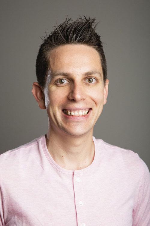 Headshot of Carlos Santana in a pink shirt with a grey background.