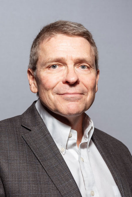 Headshot of Greg Smoak in a white button up shirt and a grey blazer.