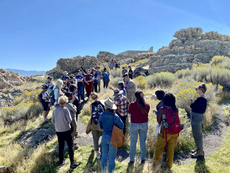 Attendees to symposium gather on a trail at Antelope Island near rock features and plants. They listen to Shoshone leaders.