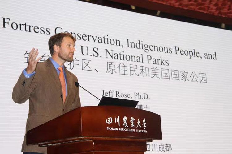 Jeff Rose stands in front of a presentations screen, that reads Fortress Conservation, Indigenous People, and U.S. National Parks