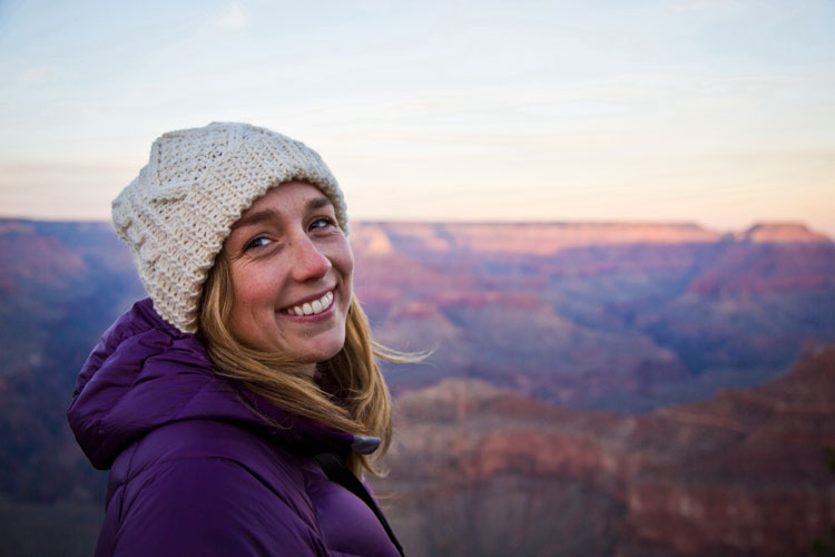 Morgan smiles in front of a Colorado Plateau landscape. She wears a purple puffy jacket and a cream colored beanie.
