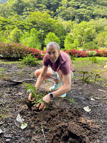 Chris kneels in a garden planting a seedling.