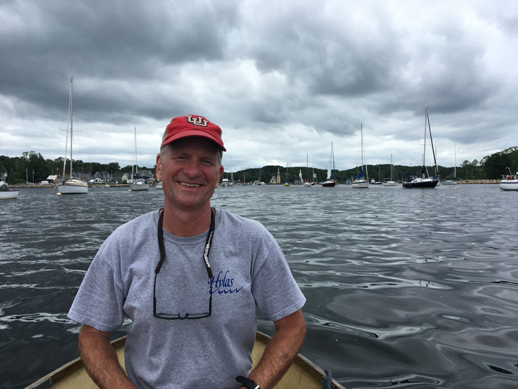 Jeff on a small sail boat in a marina. He's wearing a red U of U cap and a short sleeve grey tshirt.