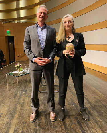 Jeff in a suit on stage standing next to Rebecca Solnit accepting the Utah Award in the Environmental Humanities.