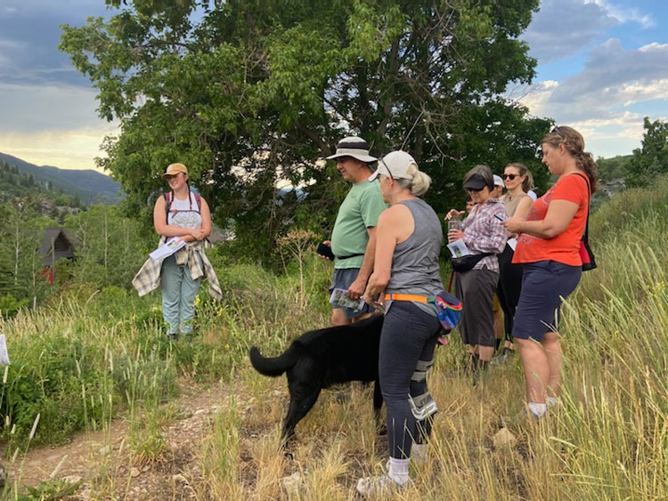 Tessa and a group of adults stand together on a trail with grasses and trees in the background.