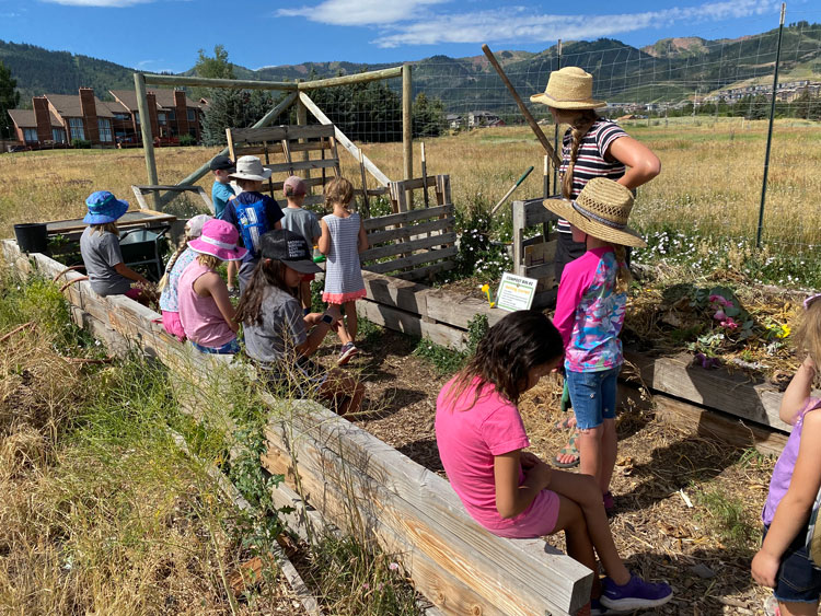 Tessa stands supervising a group of kids playing in garden beds.